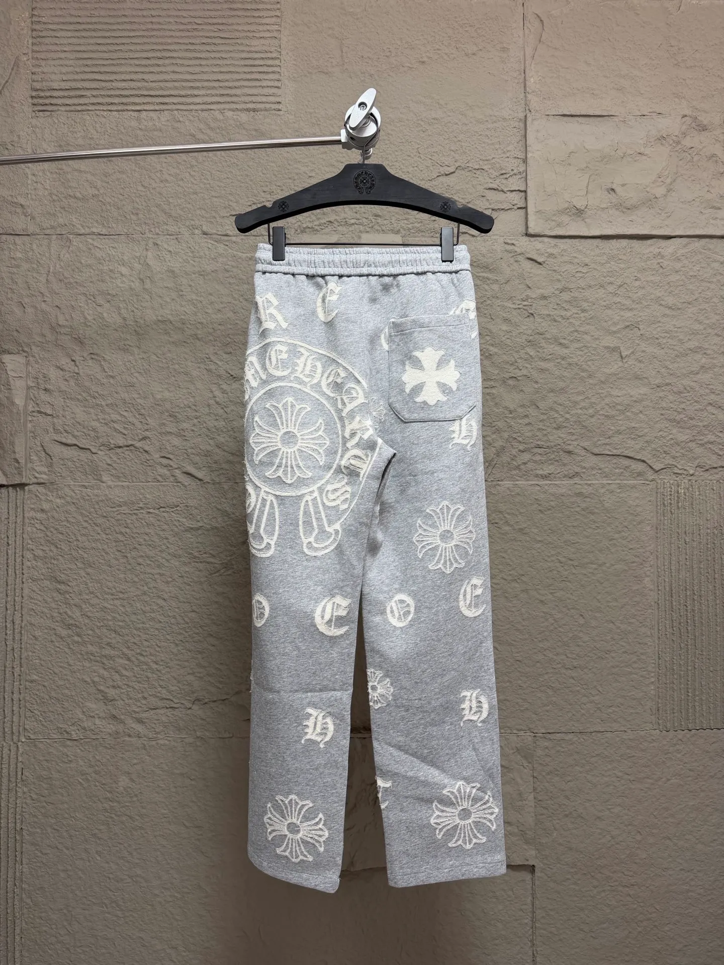 CH/Cro Heart 2026ss Burnt Flower Straight-leg Sweatpants Classic heavy-weight sweatpants with gray tones, Retro street style full-fitting, direct recognition, same style for men and women. ●Three-dimensional patchwork technology: The whole body is covered with Gothic letters + cross flower totems, using raw edge patchwork embroidery, with a mustache-like old texture, and uneven and layered patterns. It is not an ordinary print, and it is durable and not easy to fall off. ●Style tailoring: Loose, straight and wide-legged version, modifying the shape of the legs, hiding the flesh neatly, not flattering the figure, with an online drape, and the upper body has a relaxed street tone. ●Fabric and waist: Heavy knitted terry fabric, thick and soft, with good drape; elastic drawstring waist, with branded metal engraved rope ends, easy to put on and take off, and strong waist adaptability. ●Detailed design: The side pockets are convenient for carrying items, and the back pocket is decorated with cross-pattern patches. The front and rear patterns echo each other. Every detail is highly recognizable to the brand. ●Wearing scenarios: Suitable for street wear, daily outings, and trendy wear. Paired with sweaters, denim jackets, and leather jackets, you can easily create an American retro cool style. ●The overall gray base is paired with Cream White patches, which are low-key yet impactful. They are both comfortable and trendy. Versatile sweatpants, a must-have for fashionistas, are also available at the counter. SIZE：M L XL XXL XXXL